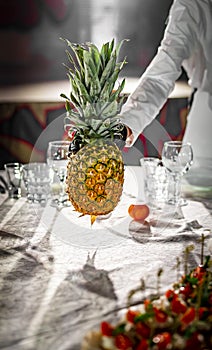 The waiter`s hands are holding a pineapple. Restaurant service