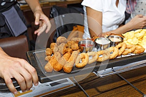 The waiter serves in the bar various snacks, beer and sauces. Chicken nuggets, chips, onion rings, fried chicken wings on a wooden