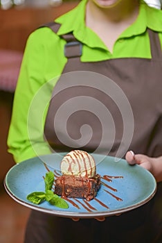Waiter serves chocolate brownie with vanilla ice-cream and chocolate caramel sauce in a blue plate. Delicious dessert.