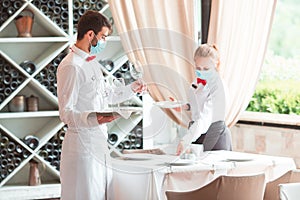 The waiter serves a table in a cafe in a protective mask