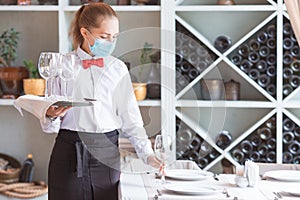 The waiter serves a table in a cafe in a protective mask