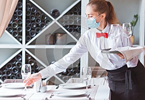 The waiter serves a table in a cafe in a protective mask