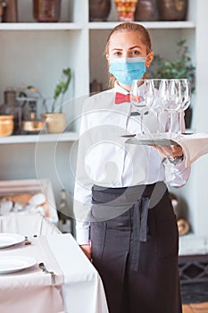 The waiter serves a table in a cafe in a protective mask