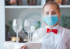 The waiter serves a table in a cafe in a protective mask