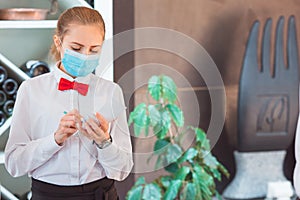 The waiter serves a table in a cafe in a protective mask