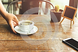 Waiter serving cup of coffee in with cell phone on cafe table.