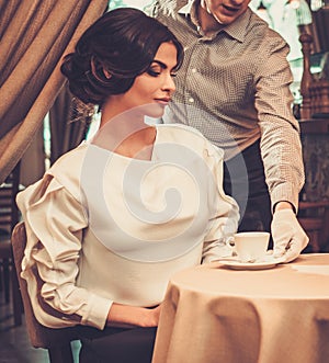 Waiter serving cup of coffee to beautiful woman