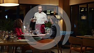 Waiter serving hungry couple in fancy restaurant. Man putting plates on table.