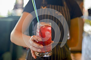 Waiter serving red alcohol cocktail. Seasonal summer drink. Young waitress at work in restaurant or cafe.