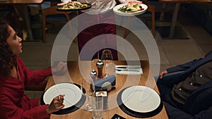 Waiter serving restaurant food to multiethnic couple at romantic dinner date.