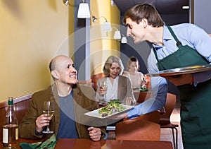 waiter serving senior male customer in cafe