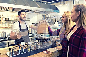 Waiter serving takeaway food to customers at counter in small family eatery restaurant