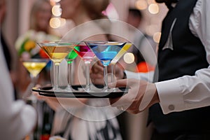 waiter serving tray of colorful martinis to guests at an upscale event