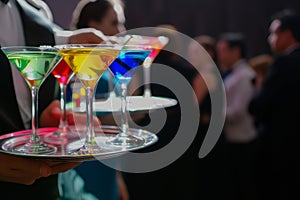 waiter serving tray of colorful martinis to guests at an upscale event