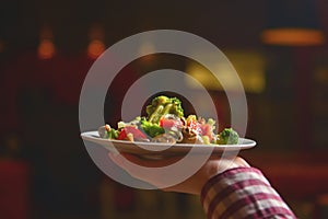 Waiter serving vegetable salad with juicy tomatoes, lettuce, radish, cucumber. Restaurant service.