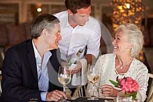 Waiter Serving Wine To Senior Couple In Restaurant