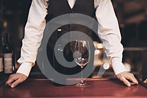 Waiter stands before tray with bottle of wine and empty glass in restaurant. Wine tasting concept.