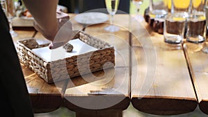 Waiter takes glass and paper napkin from wooden table with drinks and pine cone.