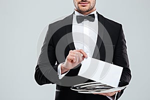 Waiter in tuxedo with bowtie holding blank card on tray