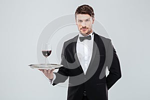 Waiter in tuxedo holding glass of red wine on tray