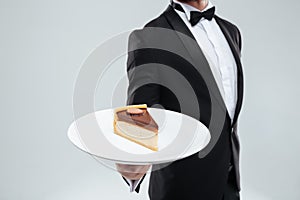 Waiter in tuxedo holding plate with piece of cake