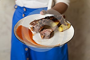 Waiter in uniform holding a plate of rack of lamb with potato gratin and sauce. Italian cuisine in a restaurant.