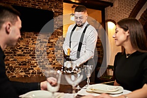 The waiter in uniform offers visitors wine in restaurant