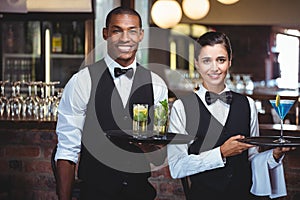 Waiter and waitress holding a serving tray with glass of cocktail