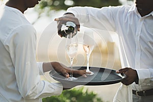A waiter in a white shirt pours champagne into a glass.
