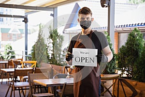 The waiter works in a restaurant in a medical mask, gloves during coronavirus pandemic