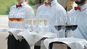 Waiters greet guests with alcoholic drinks. Champagne, red, white wine on trays