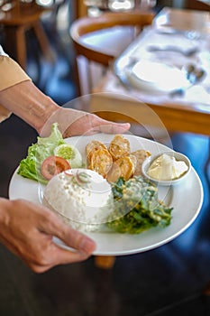 waiters in Indonesia carry white plates containing the food that will be served. the food consists of vegetables, meat and