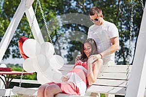 Waiting baby. pregnant woman with beloved husband sit on a bench. Husband hand embraces a round belly wife. Parenthood