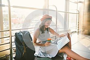 Waiting, delayed transport in the terminal of the airport or train station. Young caucasian woman in dress and hat sits on tourist