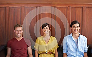 Waiting isnt a problem. Portrait of three positive-looking young people sitting on a sofa.