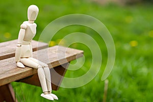 Waiting, loneliness concept. The figure of a man sits on a bench against a background of green grass. Place for text