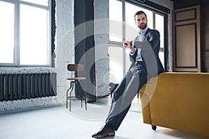 Waiting for a meeting. Serious handsome businessman weared in fashionable suit is looking at watch and waiting