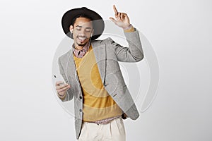 Waiting to sing along with chorus. Good-looking satisfied male model in fashionable clothes and hat, dancing with raised