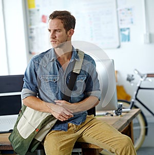 Waiting for traffic to subside before leaving work. A young man with a satchel bag sitting on his desk while looking out