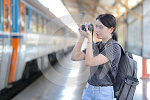 While waiting for a train, a young foreign female visitor carries a camera to take pictures