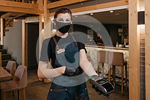 A waitress in a black medical face mask is holding a wireless payment terminal