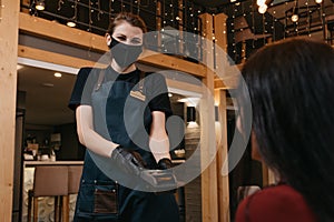 A waitress in a black medical face mask is holding a wireless payment terminal