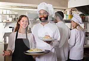 Waitress and crew of professional cooks posing at restaurant