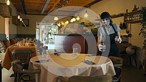Waitress with face mask and gloves setting a table of a restaurant