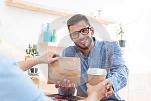 waitress giving coffee to go and paper bag with take away food to smiling young client