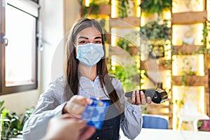 Waitress holding credit card reader machine and wearing protective face mask with client holding credit card. Man hand of customer