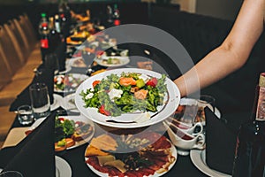 Waitress is holding fresh salad in her hand. Woman sets the table at the restaurant. Cafe service for birthday or wedding