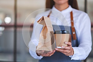 A waitress holding and serving coffee and takeaway food in paper bag to customer in a shop