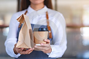 A waitress holding and serving paper cup of coffee and takeaway food in paper bag to customer in a shop