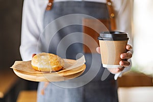 A waitress holding and serving a piece of homemade donut and a paper cup of coffee